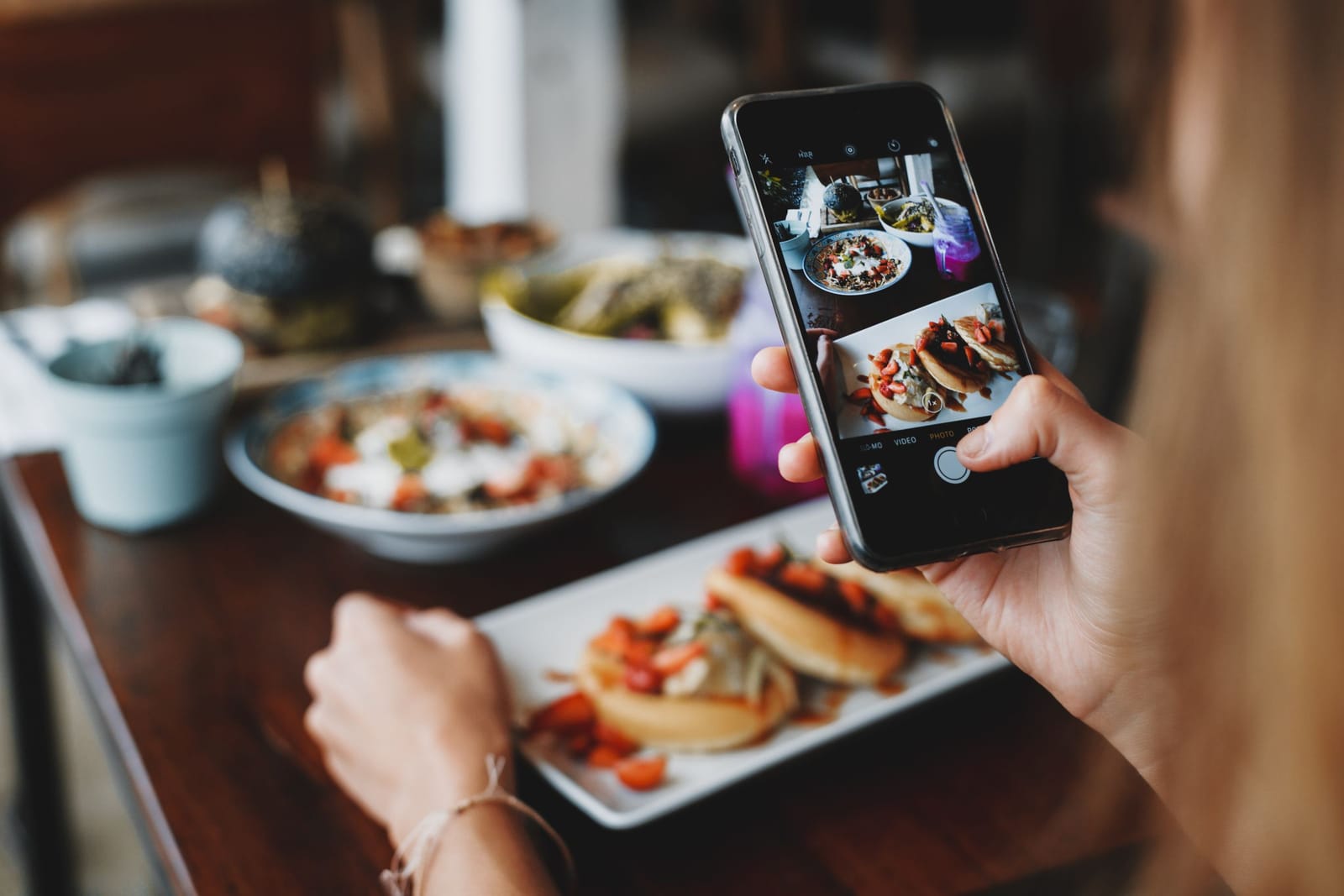 Mãos fotografam com o celular os pratos servidos na mesa de um café