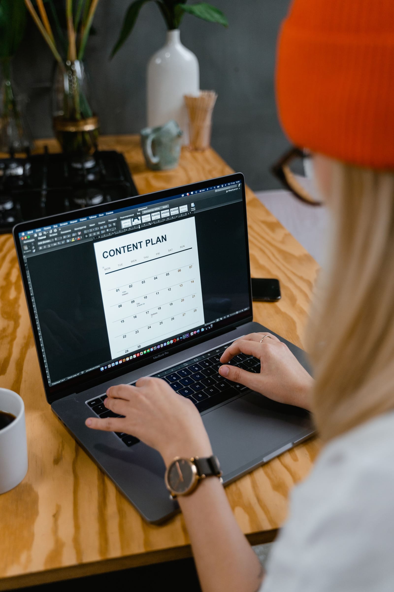 Mulher de gorro laranja digita no notebook um plano de conteúdo em formato de calendário